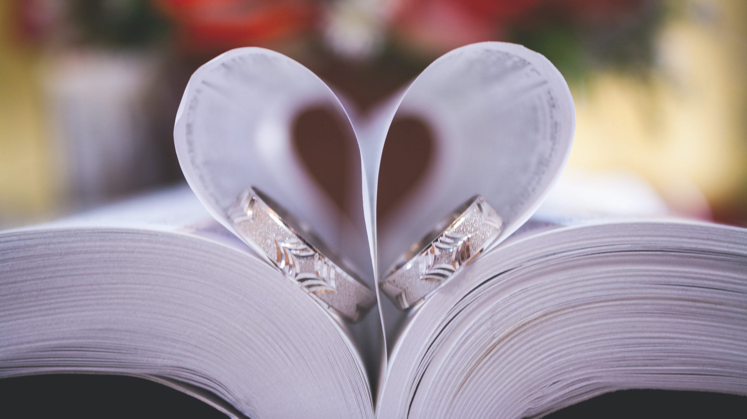 Two wedding rings nestled inside a book where the pages are shaped like a heart