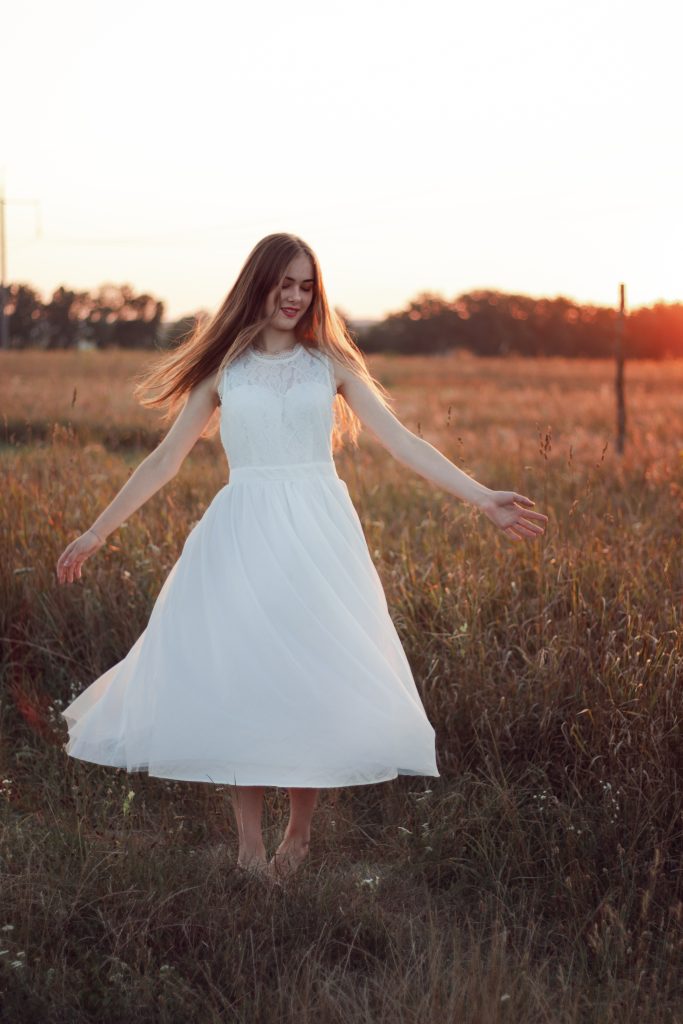 beautiful girl is dancing in a field in a pretty snow white dress